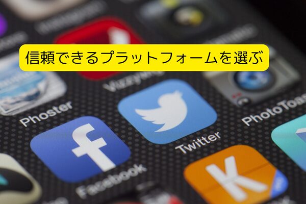 スマートフォンの画面に表示された複数のSNSアプリのアイコン。FacebookやTwitterなどの有名なプラットフォームのアイコンが目立ち、画面上には黄色のラベルで『信頼できるプラットフォームを選ぶ』というテキストが表示されている。ソーシャルメディアの選択や、信頼性の高いプラットフォームを利用することの重要性を示唆するイメージ。