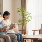50代の日本人夫婦が明るいリビングで仲良く読書を楽しんでいる様子。自然光が差し込む穏やかな雰囲気。