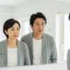 鏡の前で表情を曇らせる40〜50代の日本人男女。中年期の変化に気づいた瞬間を表現したシーン。